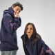 Homme et femme portant des sweats unisexes bleu marine à capuche avec des personnalisations visibles sur les manches ; une perso Homme et femme portant des sweats unisexes bleu marine à capuche avec des personnalisations visibles sur les manches ; une perso