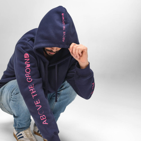 Homme accroupi portant un sweat unisexe bleu marine à capuche avec des personnalisations visibles sur la capuche et sur les deux