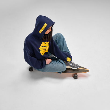 Femme assise sur une planche à roulettes portant un sweat à capuche oversize bleu marine avec une personnalisation imprimée sur 