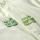 Gros plan comparant deux personnalisations en relief appliquées sur des t-shirts vert pastel au niveau de la poitrine. Gros plan comparant deux personnalisations en relief appliquées sur des t-shirts vert pastel au niveau de la poitrine.
