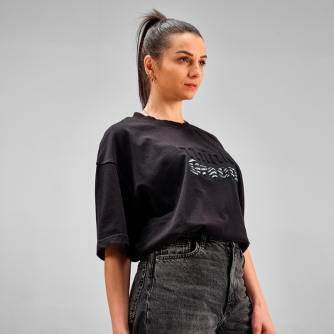 Femme portant un t-shirt oversize noir avec une personnalisation en relief et imprimée sur le devant.